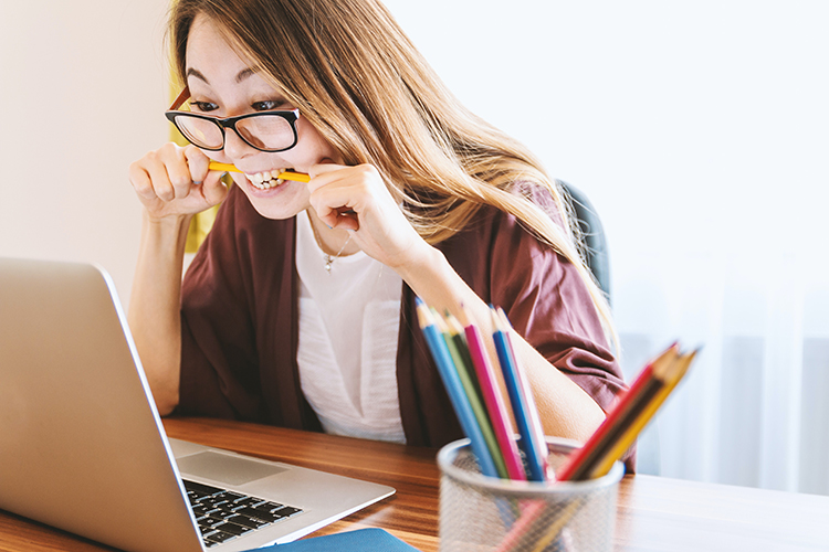 ragazza che guarda un computer mordendo una matita