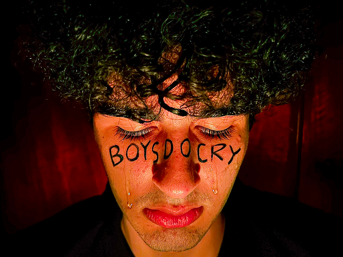 giovane uomo che piange e riporta sul viso la scritta: "Boys do cry"