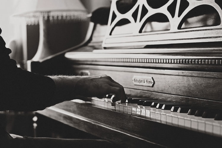 Dettaglio della locandina: mani che suonano un pianoforte